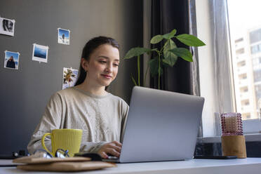 Young woman using laptop while working at home - VPIF03906