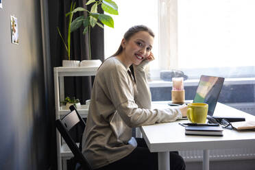 Lächelnde Frau sitzt am Laptop im Home Office - VPIF03913