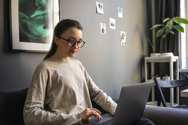 Junge Frau mit Brille arbeitet zu Hause am Laptop - VPIF03921