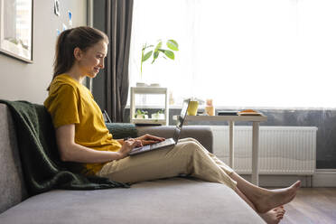 Woman using laptop while sitting on sofa - VPIF03924