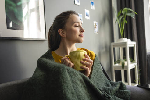 Frau in Decke eingewickelt mit Kaffeetasse zu Hause - VPIF03936