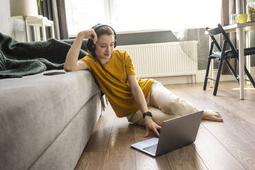 Woman with headphones using laptop while sitting on floor - VPIF03943