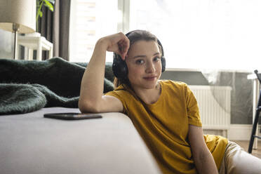 Junge Frau mit Kopfhörern, die sich an ein Sofa lehnt - VPIF03944