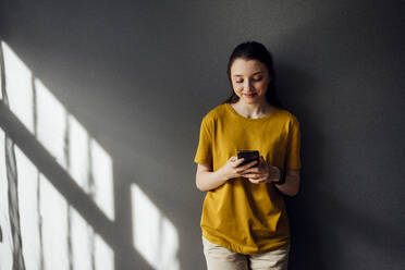 Smiling woman using mobile phone while standing at home - VPIF03952