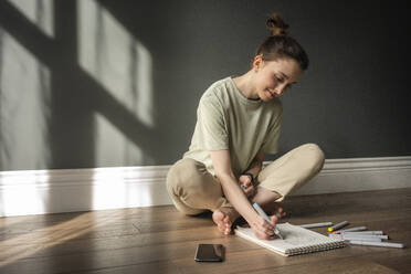 Smiling woman drawing on note pad while sitting on floor - VPIF03958