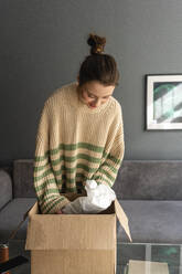 Woman unpacking box while standing at home - VPIF03973