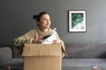 Smiling woman looking away while holding package at home - VPIF03975