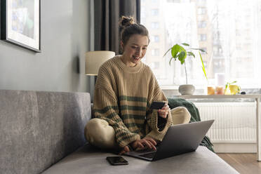 Junge Frau mit Kreditkarte beim Online-Shopping auf dem Laptop zu Hause - VPIF03978