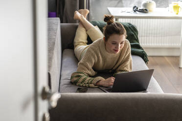 Young woman using laptop while lying on sofa - VPIF03984