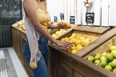 Woman with mesh bag buying lemons at supermarket - PNAF01583