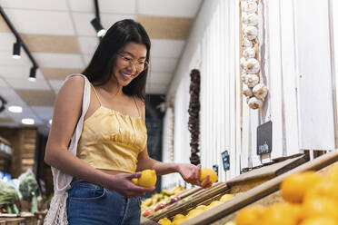 Smiling woman buying lemons at grocery store - PNAF01584