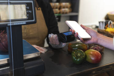 Frau hält Smartphone über Kreditkartenleser beim Bezahlen im Lebensmittelgeschäft - PNAF01593