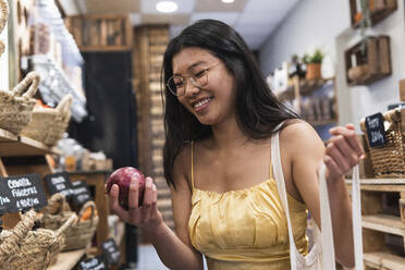 Smiling woman holding onion at grocery store - PNAF01594