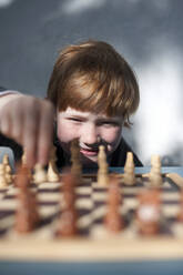 Lächelnder rothaariger Junge spielt Schach - GISF00796