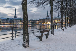 Germany, Hamburg, Illuminated city architecture reflecting in Binnenalster lake at dusk in winter - KEBF01875