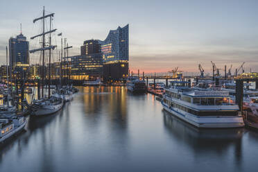 Germany, Hamburg, Boats in harbor and Elbe Philharmonic Hall illuminated at dusk - KEBF01913