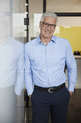 Smiling male entrepreneur standing with hands in pockets by whiteboard - RBF08079