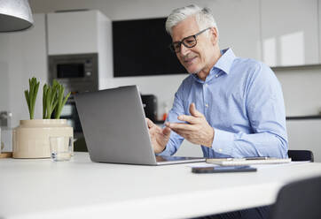 Smiling entrepreneur talking on video call through laptop in office - RBF08084