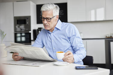 Älterer Geschäftsmann mit Kaffeetasse, der in einer Cafeteria Zeitung liest - RBF08092