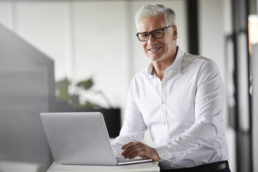 Smiling male entrepreneur with laptop in office - RBF08102