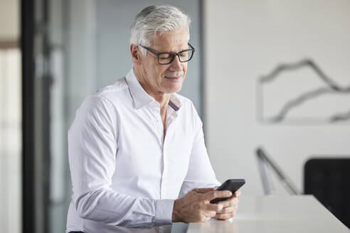 Lächelnder Unternehmer, der ein Mobiltelefon im Büro benutzt - RBF08114