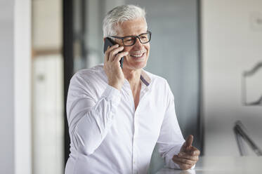 Männlicher Unternehmer mit Brille, der im Büro mit einem Mobiltelefon spricht - RBF08115