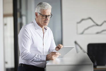 Mature professional using digital tablet while standing in office - RBF08116