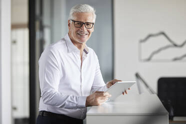 Male entrepreneur smiling while holding digital tablet at office - RBF08117