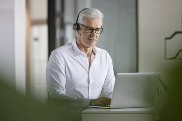 Geschäftsmann mit drahtlosem Headset und Laptop im Büro - RBF08123