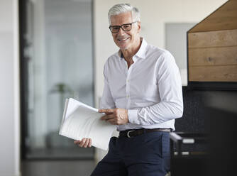 Unternehmer hält Papier und lächelt im Büro - RBF08126