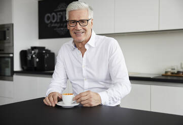 Smiling businessman wearing eyeglasses sitting with coffee cup in cafeteria - RBF08132