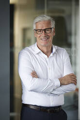 Mature male entrepreneur standing with arms crossed in office - RBF08138