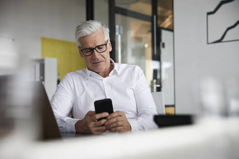 Älterer Berufstätiger, der im Büro ein Mobiltelefon benutzt - RBF08154