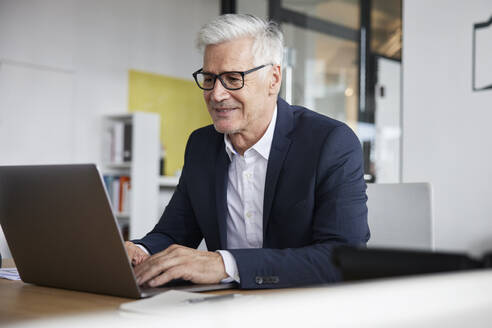 Lächelnder Unternehmer mit Laptop bei der Arbeit im Büro - RBF08166