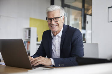 Entrepreneur with laptop smiling in office - RBF08167