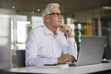 Thoughtful mature businessman with hand on chin looking away in office - RBF08173