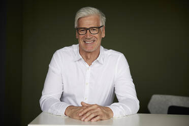 Smiling businessman wearing eyeglasses sitting in office - RBF08195