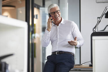 Lächelnder männlicher Unternehmer, der im Büro mit einem Mobiltelefon spricht - RBF08204