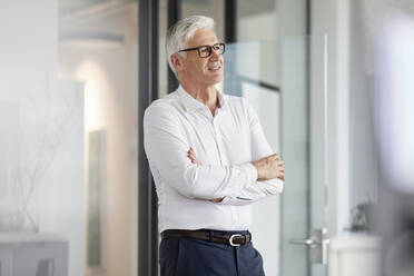 Thoughtful male entrepreneur standing with arms crossed in office - RBF08207