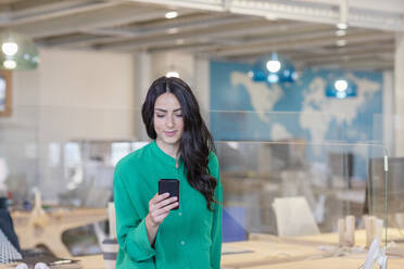 Weibliche Fachkraft, die im Büro stehend am Handy arbeitet - EIF00933