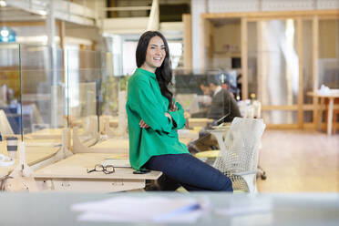 Smiling female entrepreneur looking away while sitting on desk in office - EIF00937