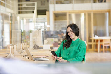 Smiling female entrepreneur using phone while sitting at desk in coworking office - EIF00939