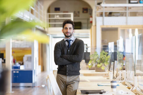 Lächelnde männliche Fachkraft mit verschränkten Armen in einem Coworking-Büro stehend - EIF00948