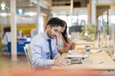 Young businessman working by female colleague in office - EIF00957