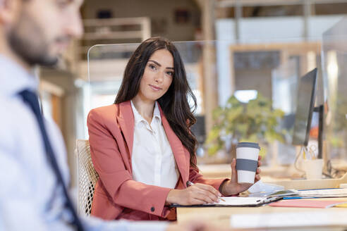 Geschäftsfrau hält Kaffee wiederverwendbaren Kaffeebecher während der Arbeit am Schreibtisch von männlichen Unternehmer im Büro - EIF00962