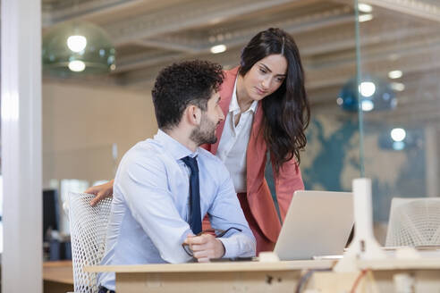 Weibliche Fachkraft schaut auf den Laptop eines männlichen Kollegen am Schreibtisch in einem Coworking-Büro - EIF00970