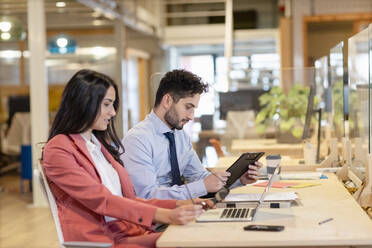 Male and female professionals working at desk in coworking office - EIF00975