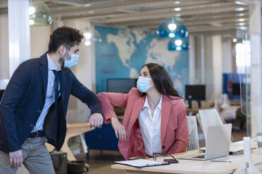 Männliche und weibliche Unternehmer stoßen sich während der Pandemie im Büro die Ellbogen an - EIF00994