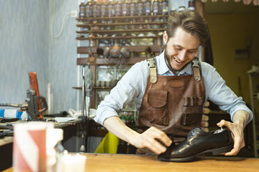 Männlicher Schuhmacher beim Polieren eines schwarzen Schuhs in einer Werkstatt - VGF00352