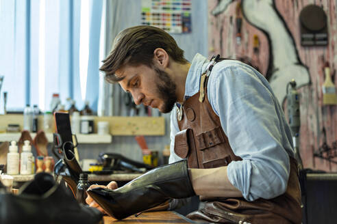 Männlicher Handwerker, der in einer Werkstatt einen Schuh repariert - VGF00364